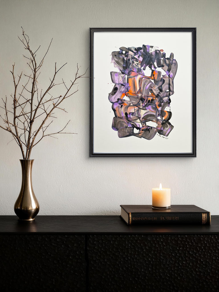 Framed abstract art piece on a wall above a dark surface with a candle and vase.