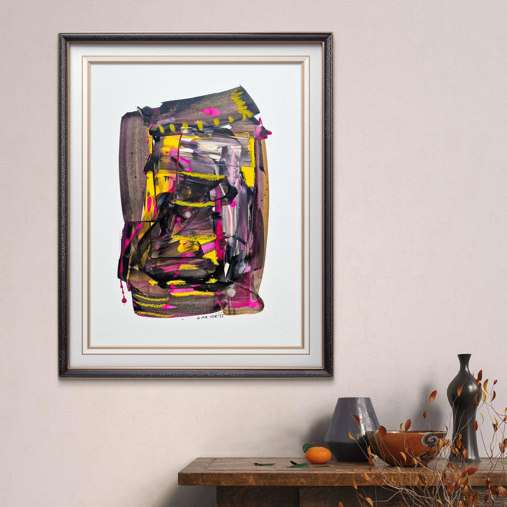 Framed abstract art piece on a wall with a table and decorative items below.