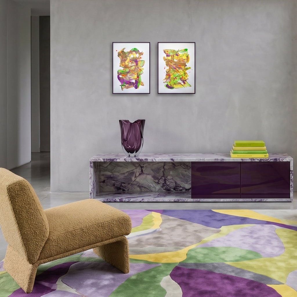 A modern living room interior featuring two abstract artworks in yellow and purple, a matching abstract patterned area rug, a textured mustard armchair, and a dark marble media console against a grey concrete wall.