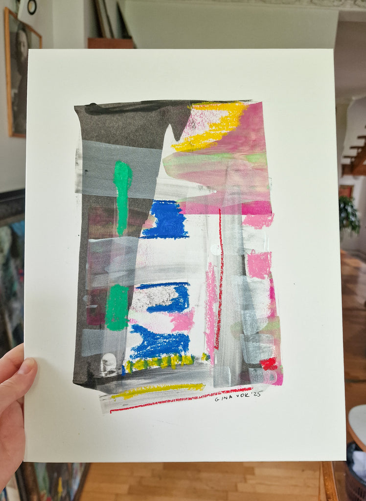 An abstract mixed-media painting on white paper, held up by a hand in an indoor setting. The artwork features a central vertical rectangular composition with layered brushstrokes and splatters of gray, black, white, pink, blue, green, and yellow.