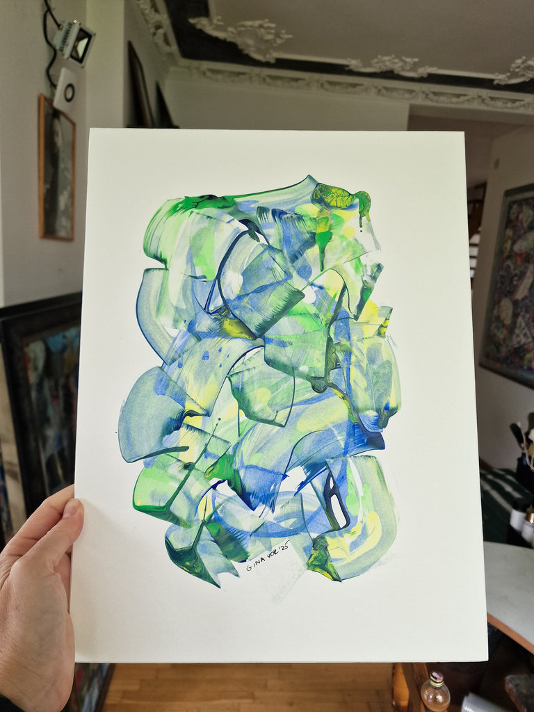 A hand holds up a artwork featuring an abstract watercolor design in shades of green, blue, and yellow, with a decorated indoor room visible in the background.