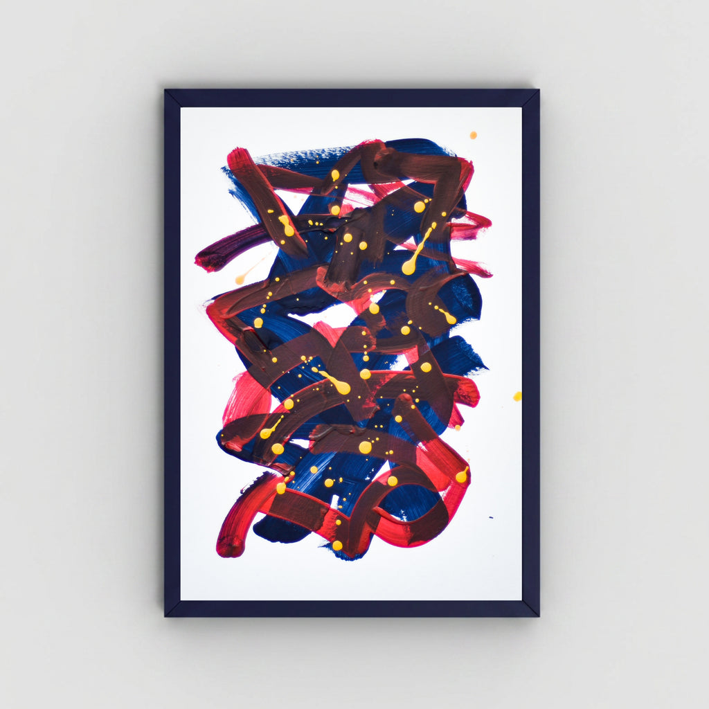A framed abstract art featuring expressive brushstrokes in navy blue, red, and dark brown with small yellow paint splatters, set against a clean white background and mounted on a light gray wall.