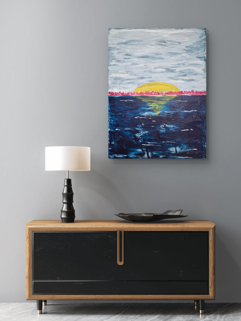 Abstract painting of a sunset over water on a gray wall above a wooden console table.