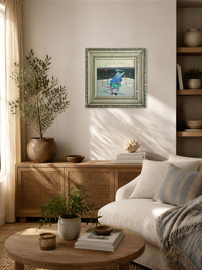 A framed abstract landscape art on a beige wall in a beautifully styled living room with a white sofa, wooden furniture, and plants.