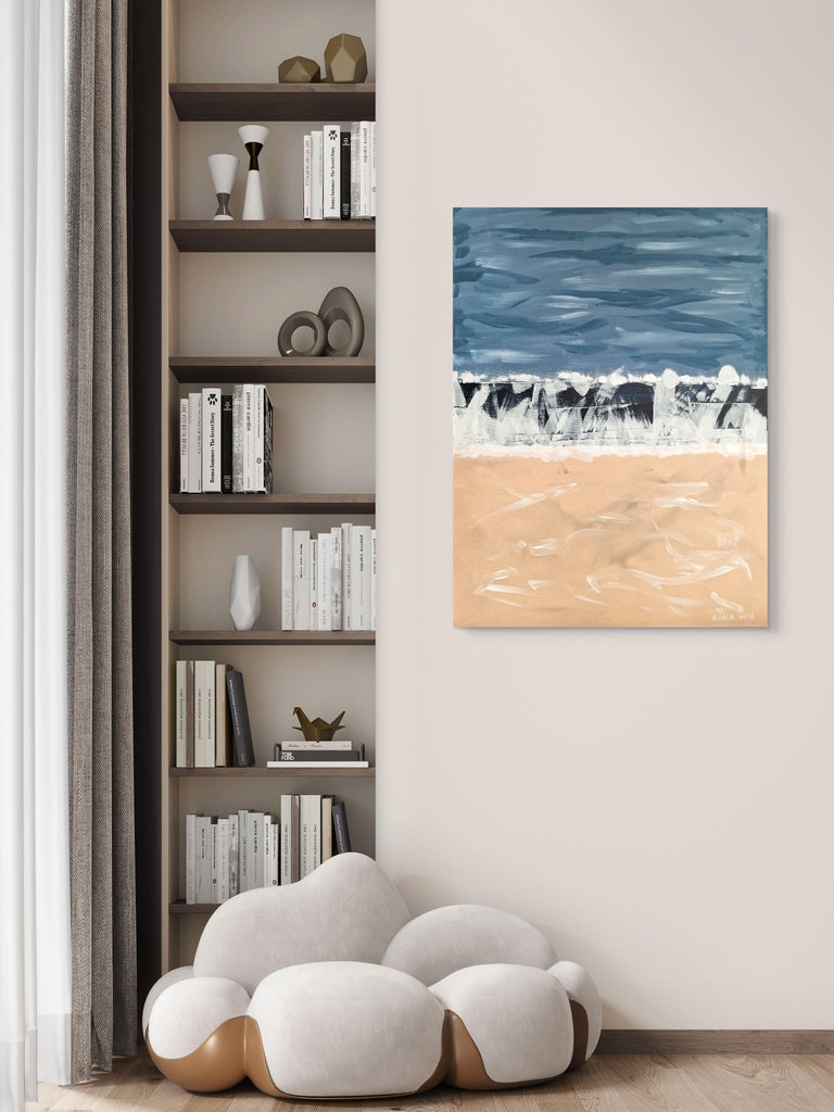 Wall art of a beach scene hanging on a wall next to a bookshelf.