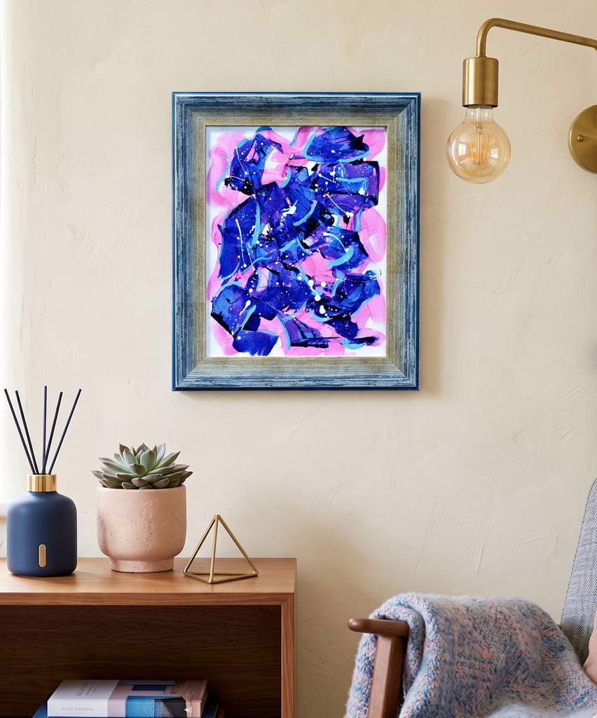 Framed abstract artwork with blue and pink colors on a wall above a wooden side table.