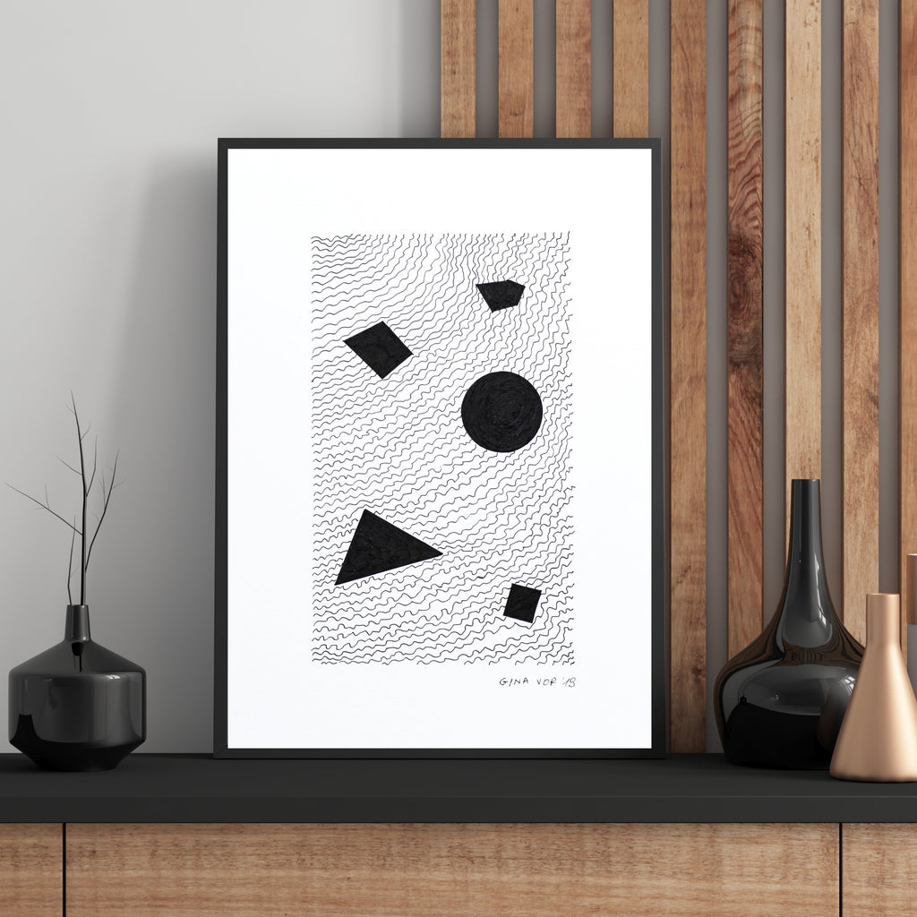 A framed abstract art with black geometric shapes on a white background with fine wavy line patterns, leaning on a wooden console against a wood slat wall with decorative vases.
