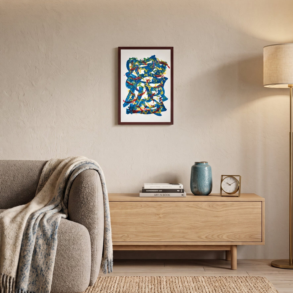 A framed abstract art with swirling blue, teal, and orange brushstrokes on a white background, hanging on a beige wall in a modern living room setting with a sofa, wooden console, and floor lamp.