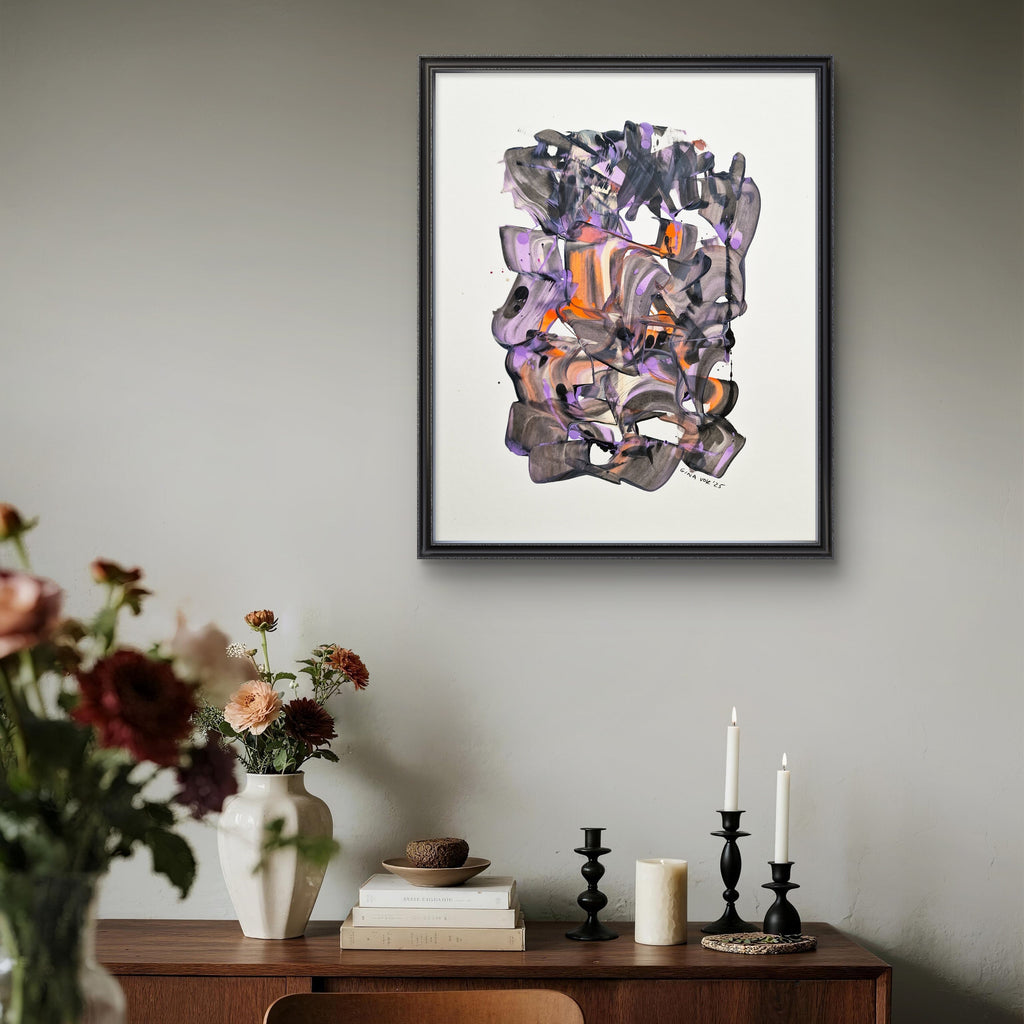 Framed abstract artwork on a wall above a wooden console table with candles and flowers.