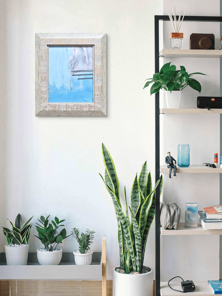 Modern interior with a bookshelf, plants, and a framed picture on a white wall.