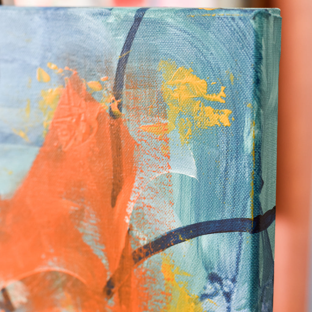 Close-up of an abstract canvas painting showing textured brushstrokes in teal blue, bright orange, yellow, and dark navy lines.