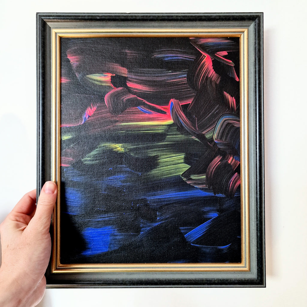 Framed abstract painting with colorful brush strokes held by a hand against a white background